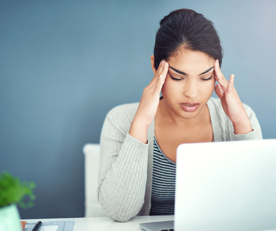 Frustrated woman holding her head in front of a laptop, showing signs of IT stress at work.