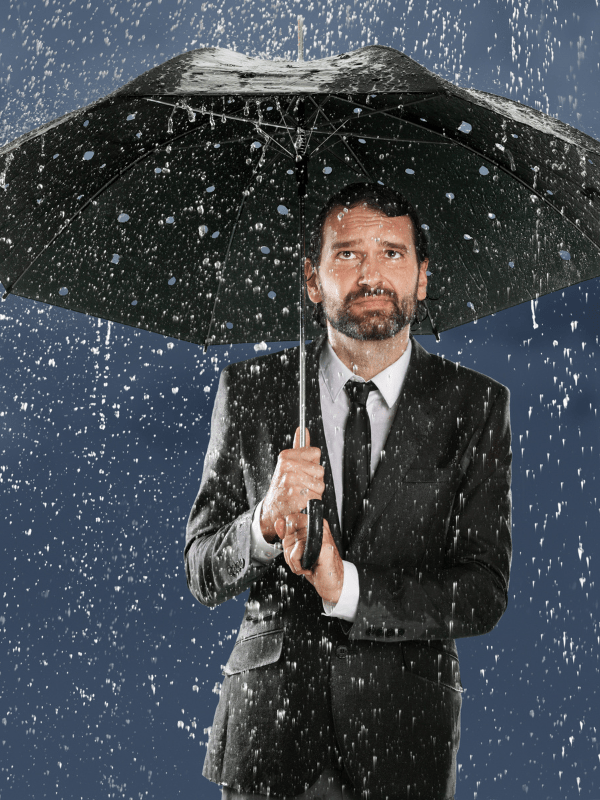 Businessman under an umbrella leaking in heavy rain, symbolizing a false sense of security