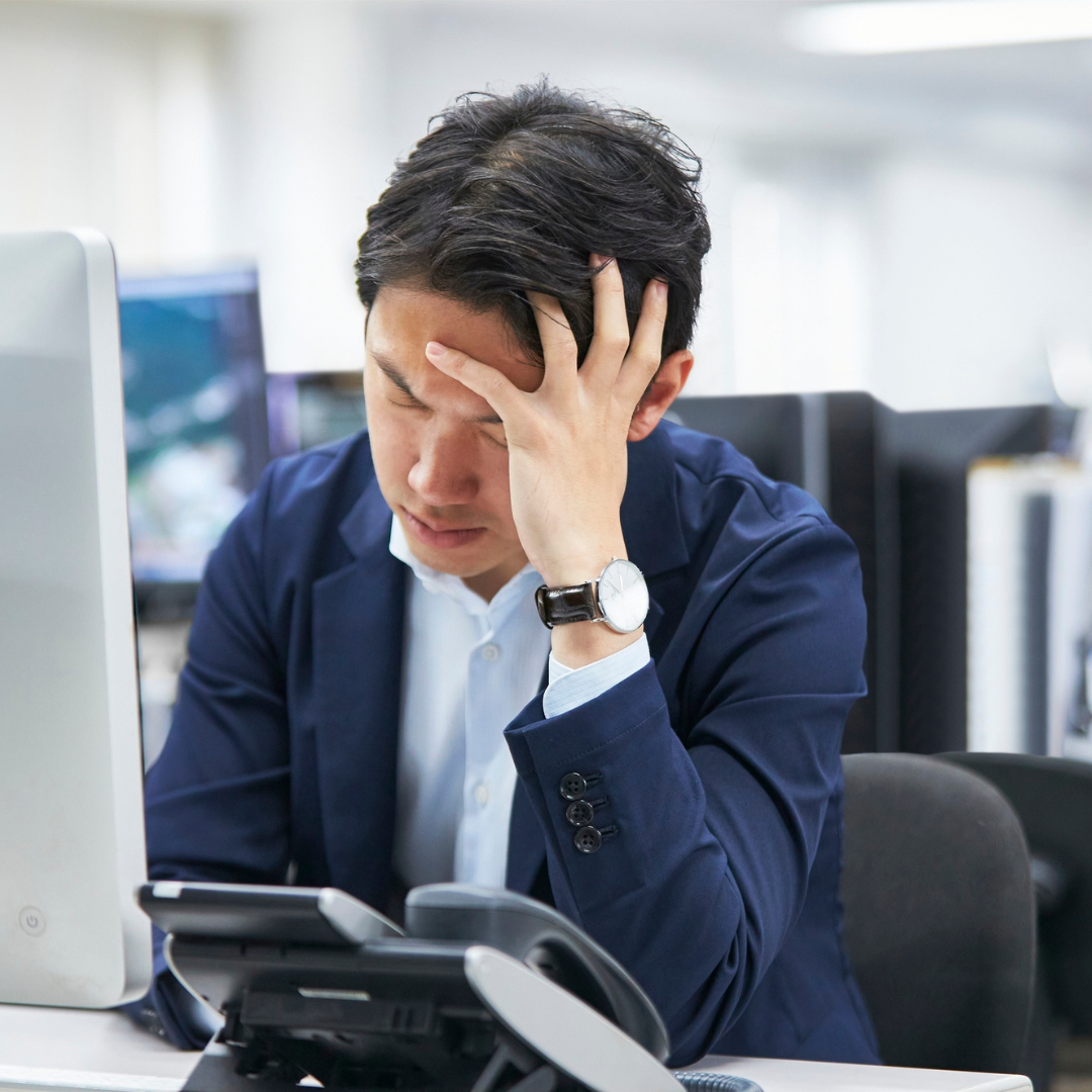 Frustrated office worker holding his head in front of a computer, overwhelmed by slow and inefficient technology at work.